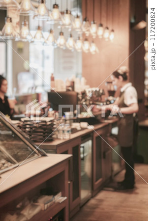 Coffee shop counter with baristas serving customers, stacks of packaged goods. Blurred background Coffee shop counter with baristas serving customers, stacks of packaged goods. Blurred background 117200824