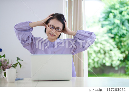 リビングでパソコンを見ながら頭を抱えるミドル女性 リビングでパソコンを見ながら頭を抱えるミドル女性 117203982
