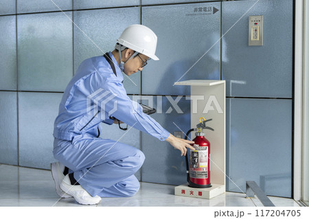 消火器の点検をする作業服の男性　ビルメンテナンス　イメージ 117204705