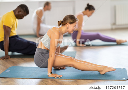 Young girl yoga teacher with multinational students performs yoga asana exercises in sport club Young girl yoga teacher with multinational students performs yoga asana exercises in sport club 117205717