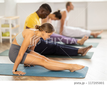 Young girl yoga teacher with multinational students performs yoga asana exercises in sport club 117205801
