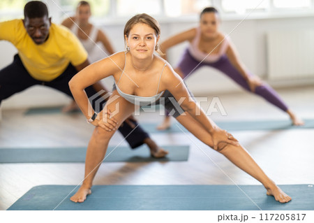 Girl conducts fitness pilates training for multinational students, performs standing exercises 117205817