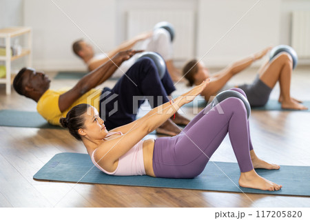 Lying and sitting on mat Asian woman coach conducts training with fitball for multinational students 117205820