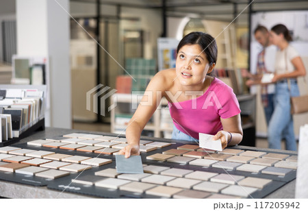 Asian woman examining tiles on sample board in home improvement store 117205942