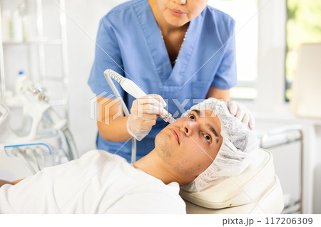 Young woman cosmetologist doing cleansing procedure to young man Young woman cosmetologist doing cleansing procedure to young man 117206309