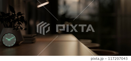 A close-up side view image of a neon alarm clock on a black table in a dark modern room at night. 117207043