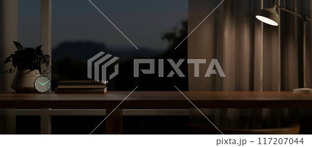 A wooden tabletop against the window in a modern dark room at night, illuminated by a table lamp. 117207044
