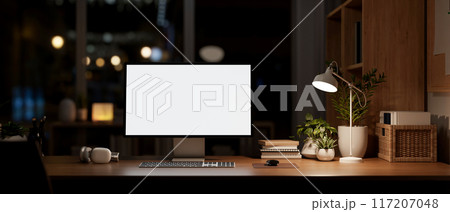 A modern dark office at night, a computer mockup on a desk, illuminated by a table lamp. 117207048