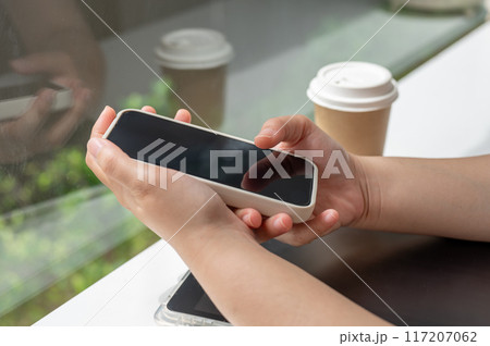 A close-up side view image of a woman using her smartphone while sitting in a coffee shop. 117207062