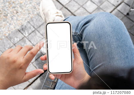 Top view image of a woman in jeans sitting outdoors, using her smartphone, touching on the screen. 117207080