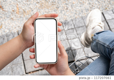 Top view image of a woman in jeans sitting outdoors and using her smartphone. 117207081