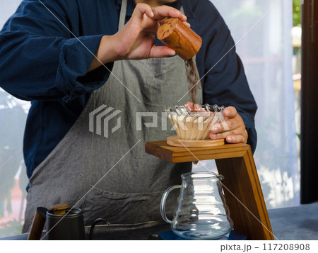 Coffee drip maker. Barista pouring ground coffee in paper filter. 117208908