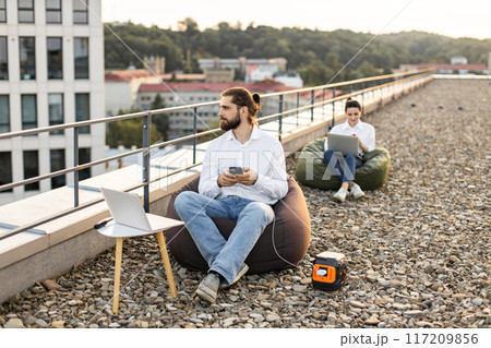 Businessman on rooftop using portable power station to charge phone 117209856