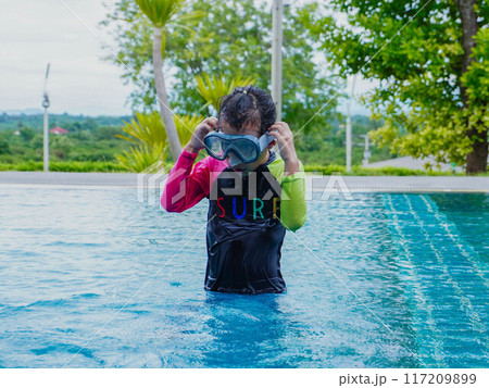 A little girl enjoys playing in the outdoor swimming pool. 117209899
