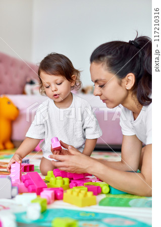 cute baby girl and her loving mother playing with colorful blocks in the children room, early development 117210316