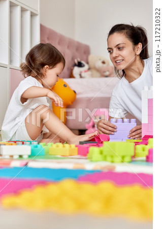 cute baby girl and her loving mother build tower from colorful cubes, having fun together 117210322