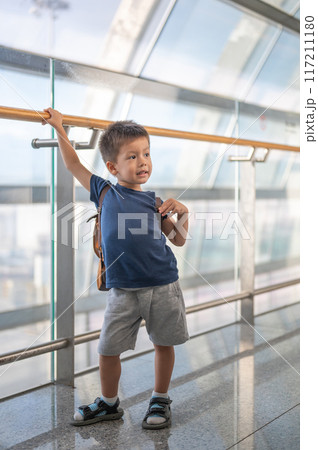 Young boy with backpack standing in modern sunlit airport terminal corridor. Young boy with backpack standing in modern sunlit airport terminal corridor. 117211180