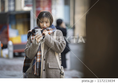 街の中でスマートフォンを見る笑顔の若い女性 117213834