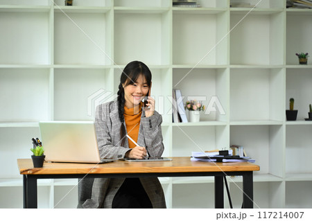 Successful asian businesswoman talking on mobile phone and using digital tablet at office desk 117214007