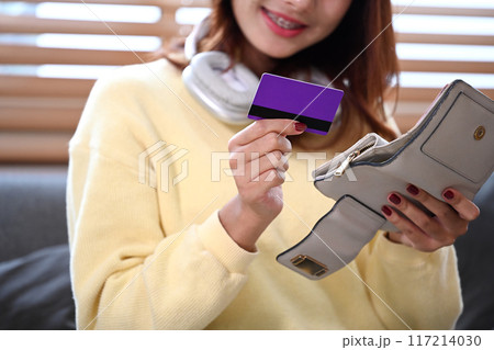 Pleased young woman holding credit card and wallet. Banking, cashless payments and online shopping concept 117214030
