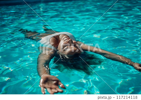 Woman relaxing swimming pool. Happy woman in a blue swimsuit floating in the pool, look form above 117214118