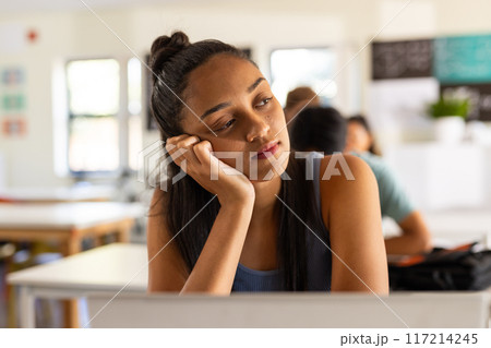 In high school, teenage girl daydreaming at desk in classroom, looking thoughtful 117214245