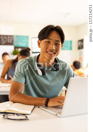 In high school, teenage boy with headphones using laptop and smiling in classroom 117214251