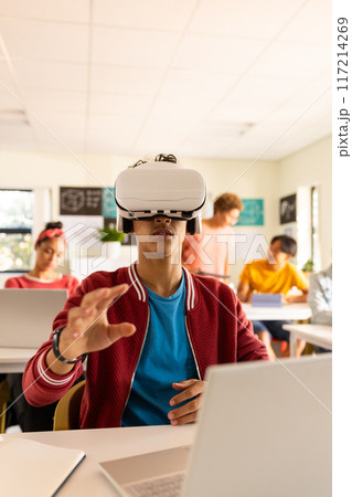 In high school, teenage boy using VR headset and laptop in classroom, exploring technology 117214269
