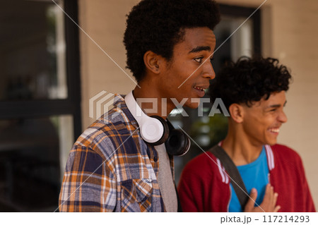 Teenage boys smiling and talking outside high school building, wearing casual clothes 117214293