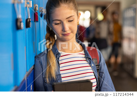 At high school, teenage girl using tablet while leaning against lockers, smiling At high school, teenage girl using tablet while leaning against lockers, smiling 117214344
