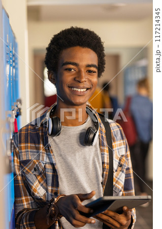 Smiling teenager holding tablet and wearing headphones in high school hallway Smiling teenager holding tablet and wearing headphones in high school hallway 117214345