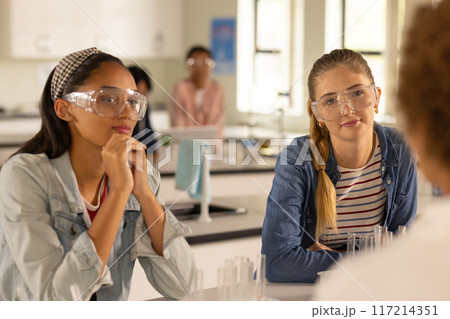 In high school, teenage girls wearing safety goggles listening in science class 117214351