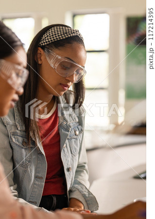 In high school, teenage girl wearing safety goggles focusing on science experiment 117214395