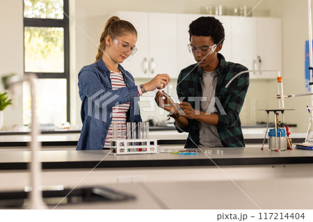 In high school laboratory, teenagers conducting science experiment with beakers and test tubes 117214404