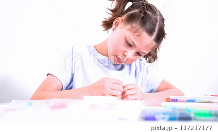 Delicate fingers of a young girl navigate through a treasure trove of bright, multicolored beads, each compartment revealing a new hue to choose from. She's immersed in the joyful task of stringing 117217177