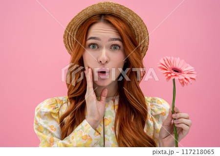 Cute young woman in straw hat with a flower in hands looking surprised 117218065