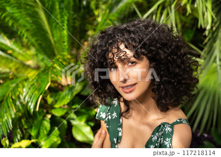 Woman with dark curly hair on a background of abstract art surrounded by lush greenery 117218114