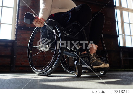 Motivational closeup of woman using wheelchair in gym and holding dumbbell in hand during strength training lit by sunlight copy space Motivational closeup of woman using wheelchair in gym and holding dumbbell in hand during strength training lit by sunlight copy space 117218210