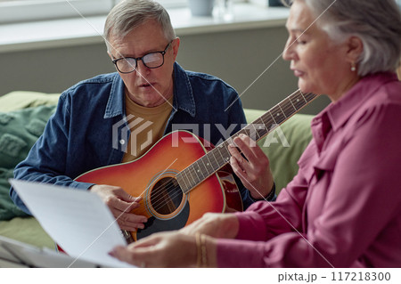 Portrait of senior man playing guitar and reading lyrics while singing song enjoying music at home 117218300