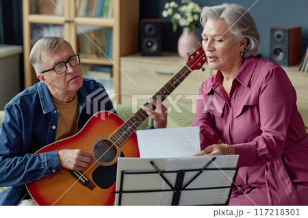 Front view portrait of senior couple singing and playing music together at home enjoying creative hobby 117218301