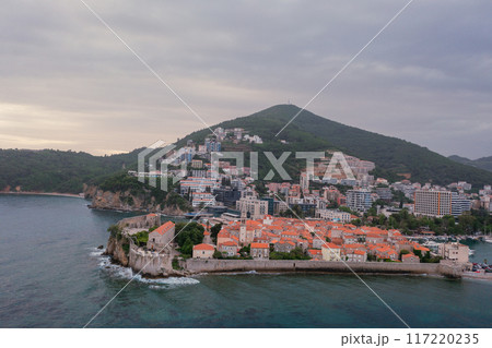Old medieval town stone houses with red roofs and church bell towers. Budva is the center of tourism in Montenegro and a summer vacation destination. Aerial drone cityscape in Montenegro. 117220235