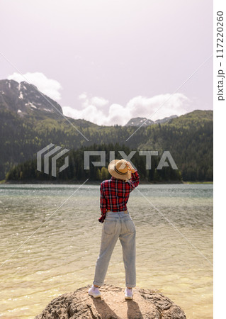 Woman traveler wearing hat and looking at amazing mountains and lake, wanderlust travel concept. black lake Montenegro. 117220260