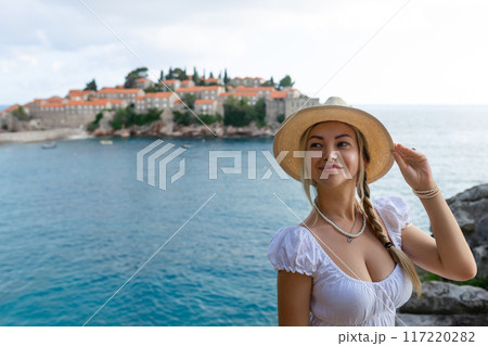 girl tourist in a hat looks from a top on the island of Sveti Stefan in Montenegro and the sea girl tourist in a hat looks from a top on the island of Sveti Stefan in Montenegro and the sea 117220282
