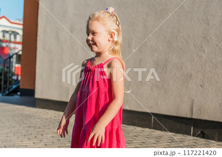 Funny baby with cochlear implant walks outdoor copy space. Hearing aid and medicine innovating technology concept. Diversity and Inclusion and people with disability concept. 117221420