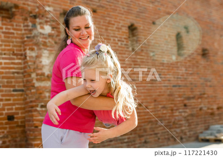 Blonde little girl with cochlear implant playing with her mother outdoor. Hear impairment deaf and health concept. Disability and inclusion. Copy space 117221430