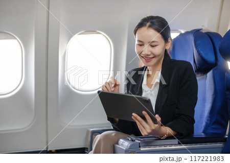 A woman is sitting on an airplane and using a tablet to write 117221983