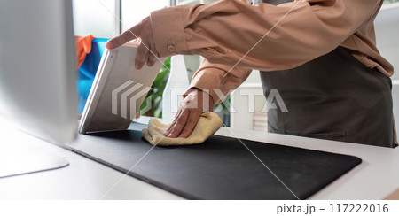 Professional Maid Housekeeper Cleaning Modern Office Desk with Cloth and Tablet in Bright Room 117222016
