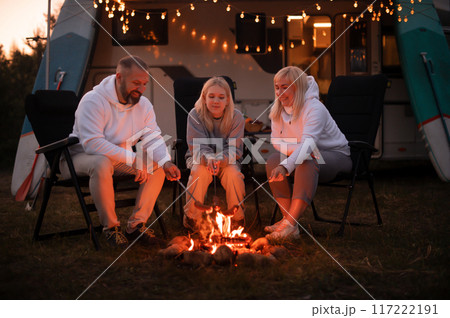 A family cooks sausages on a bonfire near their motorhome in the woods 117222191