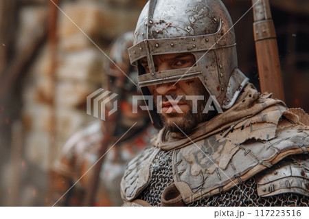 A fierce crusader warrior stands ready for battle, clad in weathered armor, as chaos unfolds in the battlefield around him. 117223516