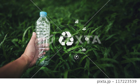 Recycle the concept of plastic water bottles,Hand holding a plastic water bottle on the grass, and an environmental icon 117223539